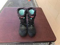 Pair of children's black winter boots from The North Face with blue interior and faux fur trim placed side by side on a table showing front view.