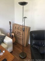 Dual floor lamp with main upward-facing bowl-shaped light and smaller task light, both in tinted chrome finish, shown near furniture.