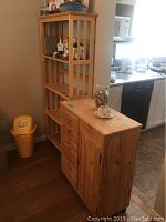 Wide side view of wooden storage cabinet with shelving unit beside it, showing top surfaces with decorative items