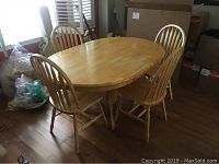 Overall view of oval wooden dining table with four matching chairs, set on wooden floor in room with windows