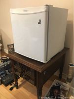 White Danby mini fridge sitting on top of a wooden end table with drawer.