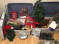 Wide view of two Rubbermaid containers filled with various Christmas decorations including small trees, wreaths, lights, bows, a nativity scene and candle decorations.