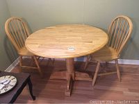 Round wooden kitchen table with two matching wooden spindle back chairs arranged around it, taken from a corner of the room.