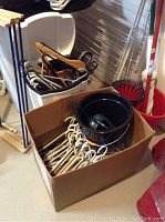 Box containing multiple plastic, wire, and wooden-coated hangers; black iron; ironing board; drying racks; mop and bucket in corner of room.