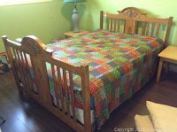 Assembled queen size bed with carved wood headboard and footboard, multicolored patchwork quilt