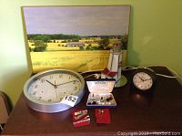 Display of cuff links, tie clips, pin, clocks, lighthouse light, and printed plaque on wooden table.
