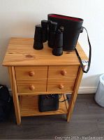 Pine night stand with two drawers shown from front, top shows binoculars and case, heater visible on bottom shelf.