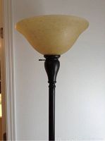 Close-up of the floor lamp showing the yellowish flared glass shade and dark metal base.