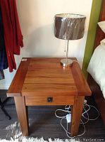 View of wood nightstand with drawer and modern lamp on top, showing natural wood grain and decorative drawer pull