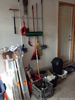 Photo showing brooms, broom handles, plastic milk crates in various colors, metal step ladders, and a black plastic garbage can