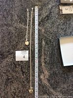 Necklace and bracelet laid on granite surface with measuring tape and lot card visible, showing lengths and style of the chains and heart pendants.