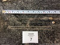 Three sterling silver lockets on chains laid out with a measuring tape, showing chain lengths up to about 20 inches.
