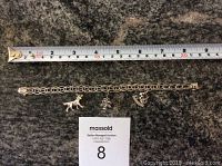 Sterling silver charm bracelet laid out flat beside measuring tape showing length.