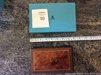 Blue Birks branded box with measuring tape showing size of music box below it on carpeted floor.
