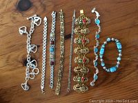 Assorted costume jewellery bracelets laid out on wooden surface showcasing variety of styles, colors and materials.