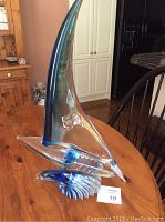 Full side view of a crystalline sailboat sculpture showing the tall curved sail with blue gradient and wave-like base.