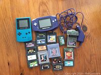 Two handheld Game Boy consoles with 17 assorted game cartridges and accessories spread on wooden floor.