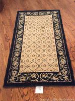 Full view of navy colored area rug on wooden floor showing the central beige panel with diamond and leaf designs and a wide navy floral border.
