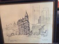 Close-up of framed ink sketch showing Toronto Flatiron building on street corner with surrounding urban buildings and streetscape, signature visible.
