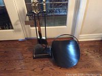 Fireplace tool set on stand with log holder on wooden floor near glass doors