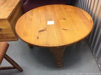 View of the round pine coffee table from above showing wood grain and wear marks including shallow nicks and bruises.