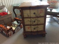Front view of small wooden chest showing three drawers with floral painted design and round metal knobs.