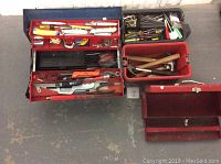 Top-down view of three tool boxes filled with assorted hand tools including saws, hammers, pliers, measuring tapes, knives, and small hardware.