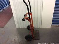 Photo of the side view showing the red frame, black handles, large wheels, and metal base plate of the hand truck dolly cart.
