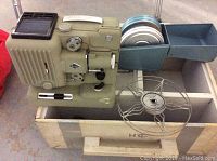 Side view of vintage movie projector showing mechanical components, film reels, and attached arm.