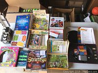 Wide view showing assortment of games including Anomia, Kingdomino, Stratego, Shopkins Monopoly, and others with opened boxes and game components visible.