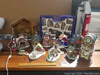 Ten-piece ceramic Christmas village with some light-up buildings and hand-painted nativity scene in box displayed on table.