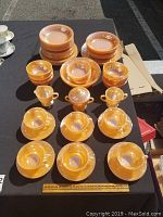 Full display of the Fire King vintage orange marbled glassware showing dinner plates, side plates, bowls, tea cups with saucers, sugar bowl with lid, and creamer.
