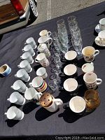 Wide overhead view of the collection showing various white mugs, some colored mugs, clear glasses, and a teapot with a brass lid.