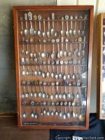 Full view of wooden display case filled with 5 rows of collectible spoons with various decorative handles