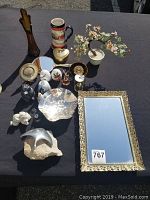 Overview photo showing assortment of decorative items on black cloth including silver bowl, mirror, plates, figurines, vase, heart box, and flower bonsai tree.