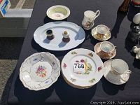 Photo showing assorted china plates and cups with floral and fruit patterns on a black table.