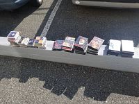 Photo showing multiple stacks of DVDs and CDs laid on a curb outside in sunlight.