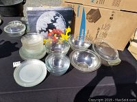 Varied assortment of clear glass kitchenware including mixing bowls, plates, and serving dishes in different sizes and styles displayed outdoors on black cloth.