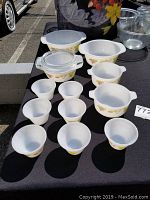 Photo of the entire vintage milk glass bakeware set including various sized bowls and baking dishes featuring a floral pattern of yellow and orange flowers on white milk glass.