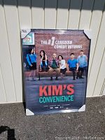 Front view of the Kim's Convenience 30x40 framed poster leaning against a wall showcasing the entire poster design including cast and title text.