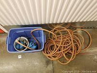 Top view of two blue Diamond submersible water pumps inside a blue container with a long orange water hose coiled and spread outside the container.
