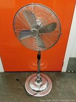 Full front view of stainless steel adjustable height oscillating pedestal fan with large circular base and power cord.