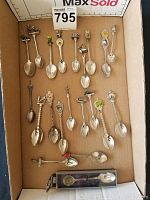 All 17 collector spoons arranged in a cardboard box. Includes variety of decorative spoon handles with themes like animals, crowns, landmarks, and a strawberry-shaped handle.
