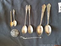 All four sterling silver spoons, pin and necklace chain laid out on dark fabric background