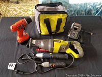 Photo shows all tools placed on a black surface with a yellow and black tool bag behind them. Items include Ryobi reciprocating saw, Black & Decker cordless drill, two powered screwdrivers, and Ryobi charger.