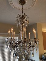 Chandelier hanging from ceiling showing eight lit candle-style bulbs and crystal drapes