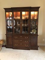 Front view of full china cabinet with interior lighting on, showing bowed glass doors and displayed items