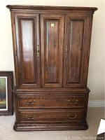 Front view of closed armoire showing three-paneled doors and two lower drawers.