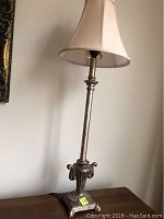 Full view of candlestick style table lamp with cream fabric bell-shaped shade on wooden surface.