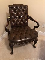 Front view of entire leather armchair showing tufted back, seat and wood frame